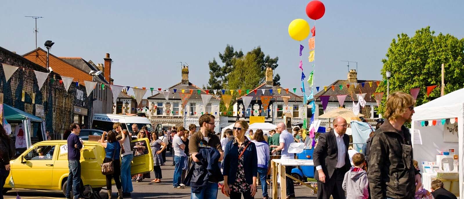 Multicoloured bunting and balloons are hung in Chapter's car park. People walk around the stalls on a sunny day.