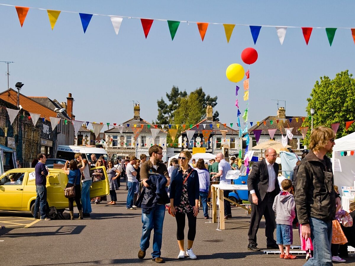 Multicoloured bunting and balloons are hung in Chapter's car park. People walk around the stalls on a sunny day.