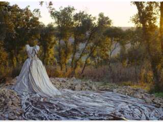 A white dress stands alone on rocky ground in a forest. The sun sets behind the dress.