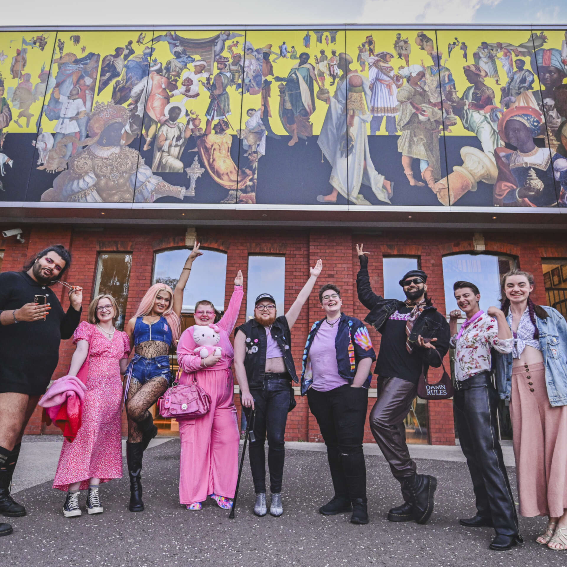 A group of people dressed in pink are stood in a line and waving their arms in front of Chapter Arts Centre.