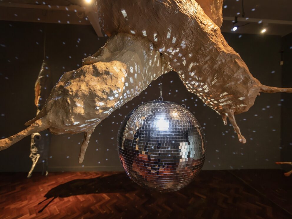 An installation view of Abi Palmer's exhibition Slime Mother, featuring two sculptures of slugs suspended above a disco ball.