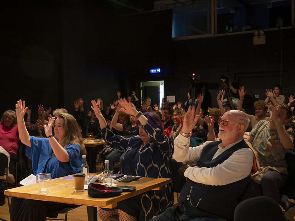 A seated audience applaud in BSL.