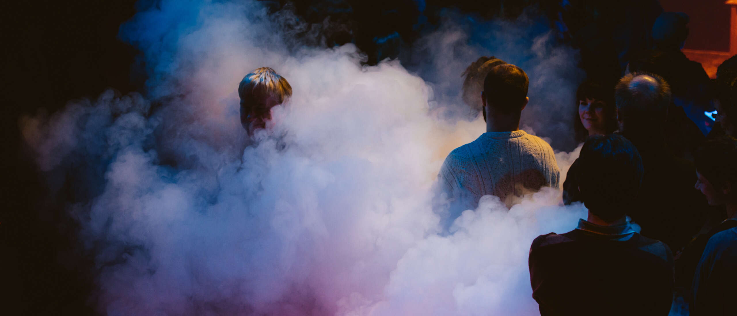 Performers are stood on stage with pink and purple smoke surrounding them.