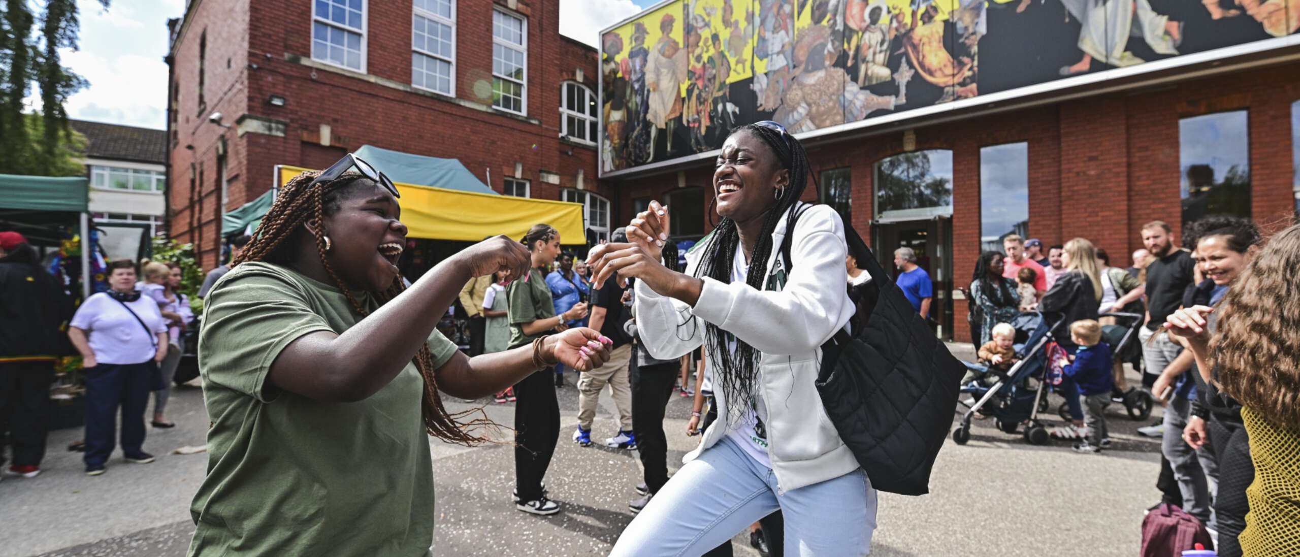 Two people dance in the forecourt of Chapter Arts Centre. There are many people in the background watching dancing, eating food and generally celebrating the Jamaica Independence Day event.