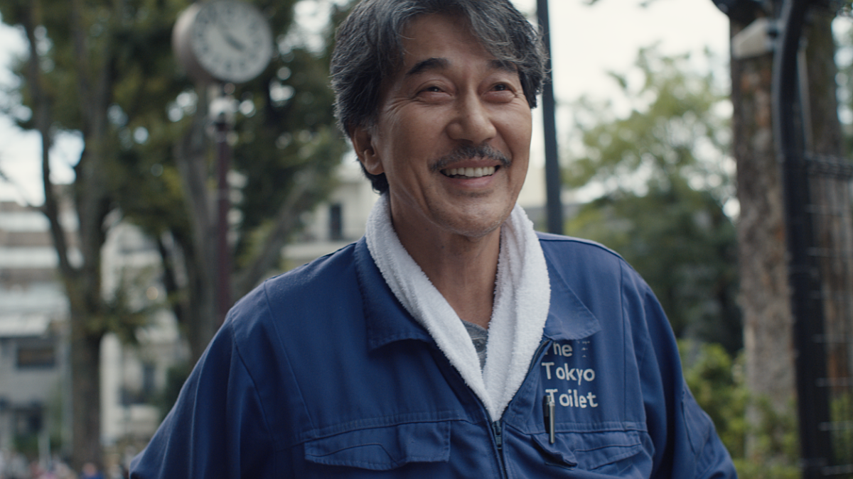 Kôji Yakusho smiles whilst wearing a blue boiler suit in the film Perfect Days.