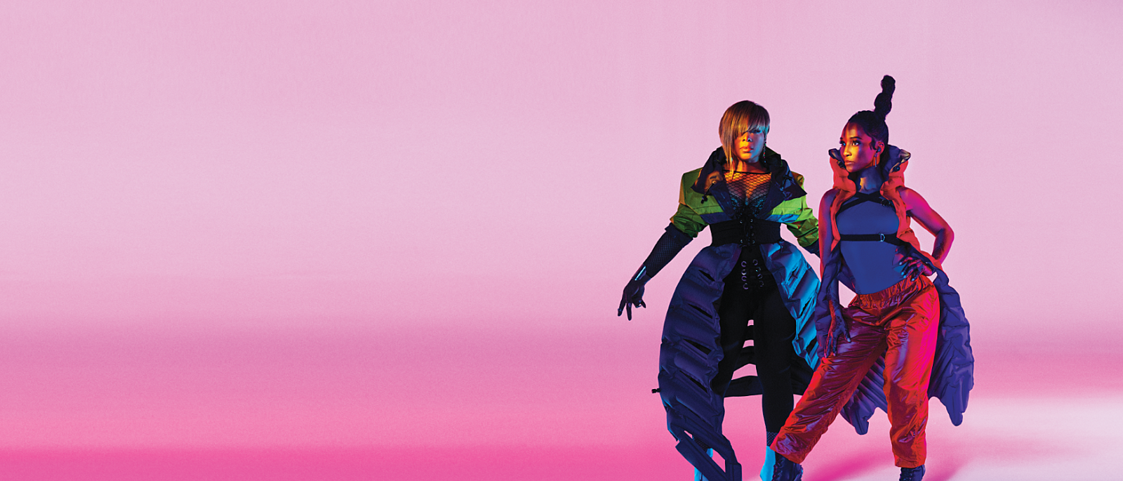 Girl group TLC pose for a photograph against a neon pink background.
